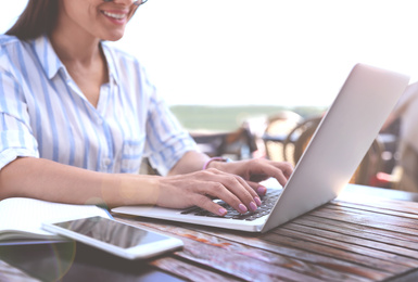 Image of Woman working with laptop at outdoor cafe on sunny day, closeup