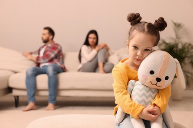 Sad little girl with toy and her arguing parents on sofa in living room