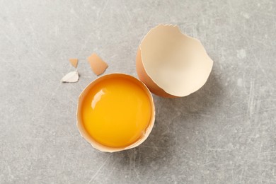 Photo of Raw yolk in broken chicken eggshell on light grey table, top view