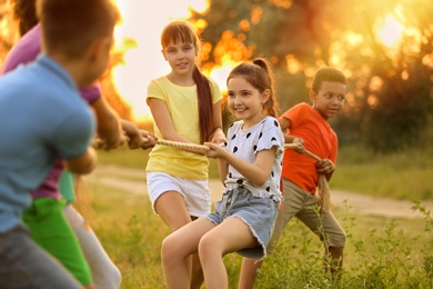 Image of Cute little children playing tug of war game outdoors at sunset