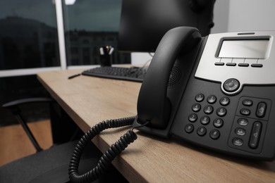 Stationary phone on wooden desk in office, closeup. Hotline service