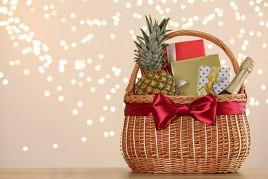 Wicker basket with gifts, champagne and food against blurred festive lights. Space for text