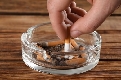Man putting out cigarette in ashtray on wooden table, closeup