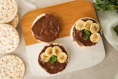 Puffed rice cakes with chocolate spread, banana and mint on grey marble table, flat lay