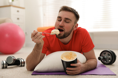 Lazy young man eating ice cream instead of training at home