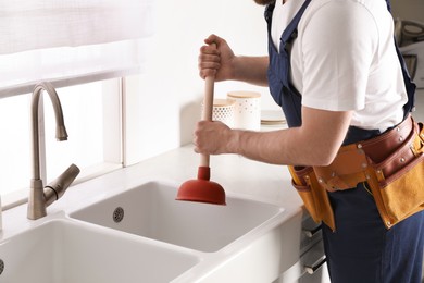 Plumber using plunger to unclog sink drain in kitchen, closeup