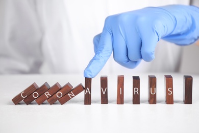 Doctor stopping domino effect at white table, closeup. Prevent spreading of coronavirus