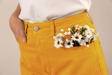 Image of Woman with beautiful tender flowers in pocket of orange jeans on light background, closeup