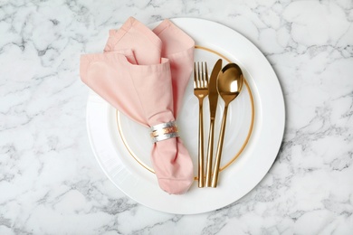 Plate with golden cutlery and napkin on marble background, top view. Festive dinner setting