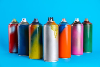 Photo of Used cans of spray paints on light blue background