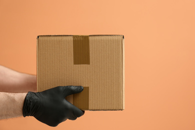 Courier holding cardboard box on orange background, closeup. Parcel delivery
