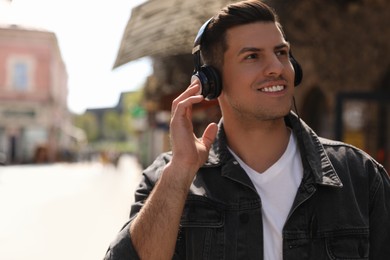 Handsome man with headphones listening to music on city street, space for text