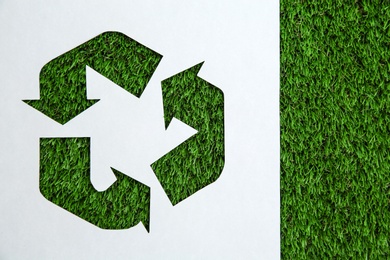 Sheet of paper with cutout recycling symbol on green grass, top view. Space for text