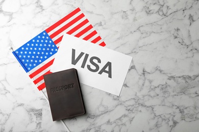 Flat lay composition with flag of USA, passport and word VISA on marble background. Space for text