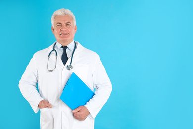 Portrait of senior doctor with clipboard against blue background, space for text