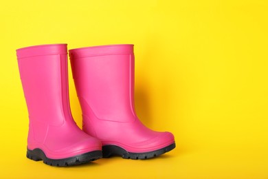 Pair of bright pink rubber boots on yellow background. Space for text