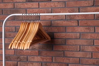Wooden clothes hangers on rack near red brick wall. Space for text