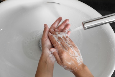 Woman washing hands with soap over sink in bathroom, top view