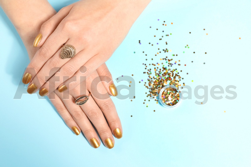 Woman showing manicured hands with golden nail polish and glitter on color background, top view