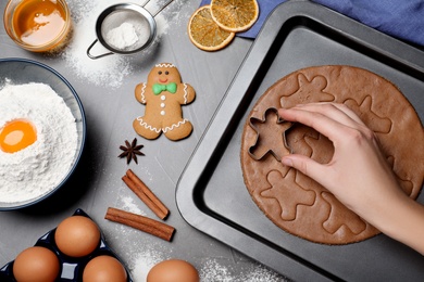 Photo of Woman making Christmas gingerbread man cookies at grey table, closeup