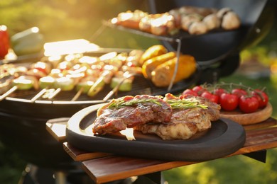 Tasty cooked meat and cherry tomatoes on table near barbecue grill outdoors