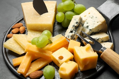 Cheese platter with specialized knife and fork on black table, closeup view