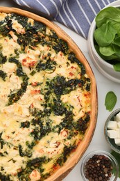 Photo of Delicious homemade spinach quiche and ingredients on white table, flat lay