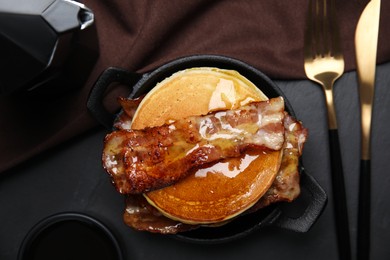 Delicious pancakes with maple syrup and fried bacon on black table, flat lay
