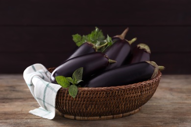 Ripe purple eggplants and basil in wicker bowl on wooden table, closeup