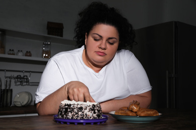 Depressed overweight woman eating cake in kitchen at night