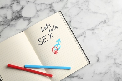 Notebook with phrase "LET'S TALK SEX" and gender symbols on marble background, top view