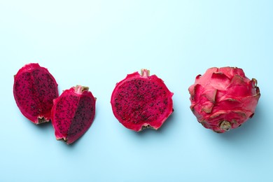 Delicious cut and whole red pitahaya fruits on light blue background, flat lay