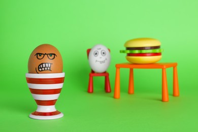 Photo of Angry egg and happy one with burger at table on green background
