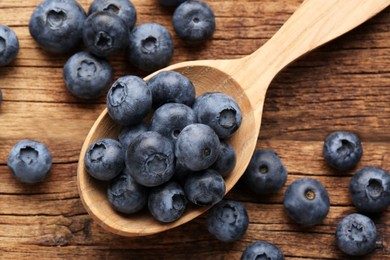 Spoon with tasty fresh blueberries on wooden table, flat lay