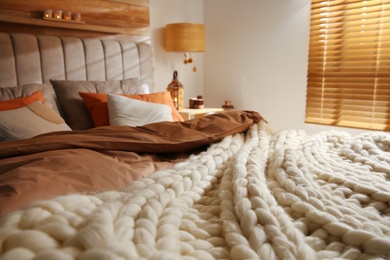 Bed with cozy knitted blanket and cushions indoors. Interior design