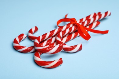 Sweet Christmas candy canes with red bow on light blue background, closeup