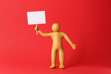 Human figure made of yellow plasticine holding blank sign on red background