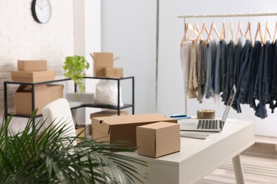 Store interior with clothing rack, cardboard boxes and laptop. Online selling
