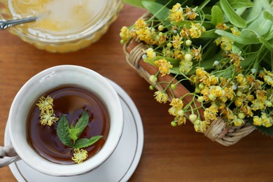 Cup of hot aromatic herbal tea, honey and linden blossoms on wooden table, above view