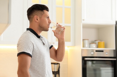 Man drinking pure water from glass in kitchen. Space for text