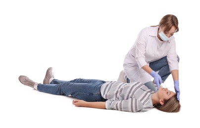 Doctor in uniform and protective mask performing first aid on unconscious woman against white background