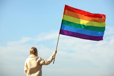 Woman holding bright LGBT flag against blue sky, back view