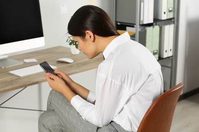 Young woman with bad posture using smartphone while sitting in office. Symptom of scoliosis