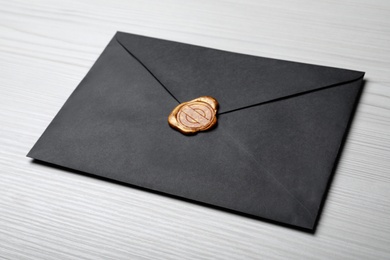 Black envelope with wax seal on white wooden background