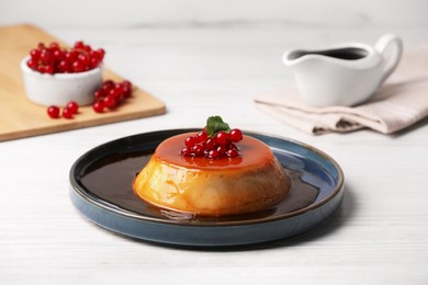 Photo of Plate of delicious caramel pudding with red currants and mint on white wooden table