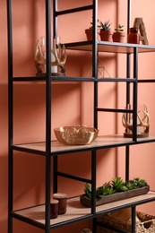 Shelving with different decor and houseplants near coral wall. Interior design