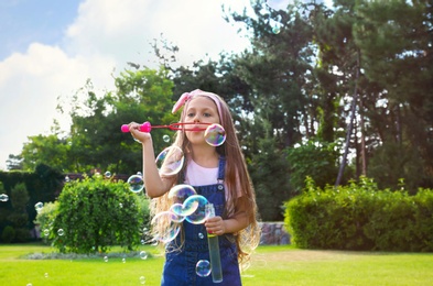 Cute little girl blowing soap bubbles in green park