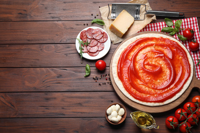 Flat lay composition with base and ingredients on wooden table, space for text. Pepperoni pizza recipe