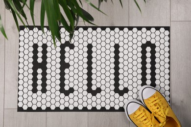 Stylish door mat with word Hello, shoes and houseplant on floor, flat lay