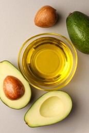 Photo of Cooking oil in bowl and fresh avocados on light grey background, flat lay